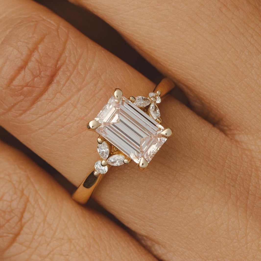 Gold band engagement ring with emerald cut center diamond and marquise side stones on hand