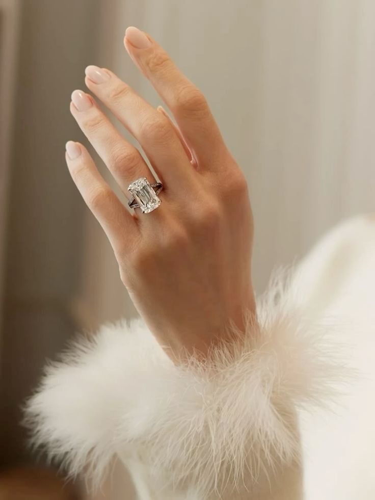 Emerald cut diamond engagement ring on hand with white feathered sleeve, fine jewellery