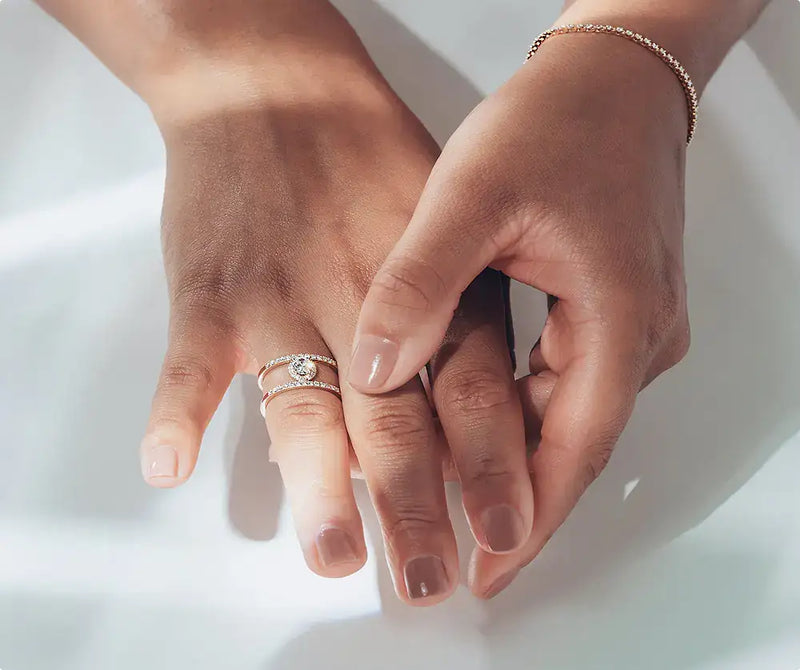 Hand with lab-grown diamond engagement ring and gold bracelet on light background