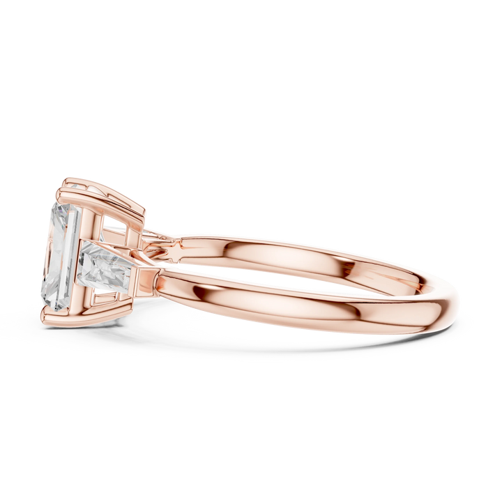 Side profile of rose gold trinity ring with emerald center stone and radiant side diamonds